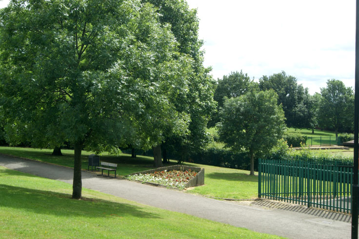 A bed of plants with a bench and bin on the left, and a fence on the right.